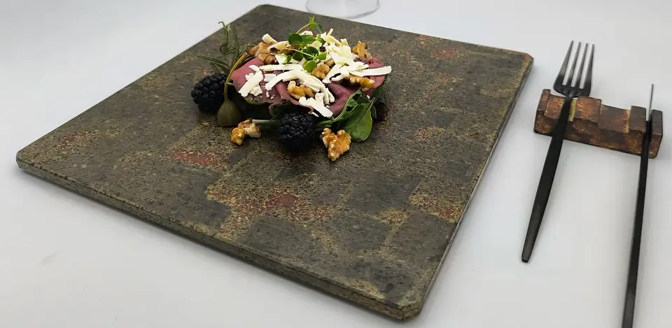 Piatto quadrato in pietra lavica con finitura materica nei toni naturali e composizione gastronomica