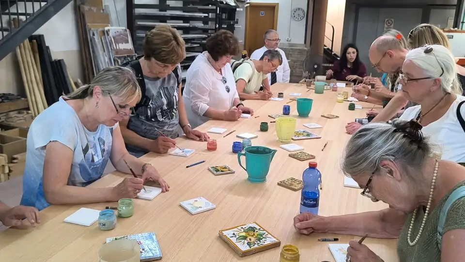 Partecipanti dipingono piastrelle al tavolo del laboratorio Artesole