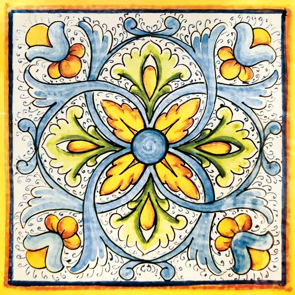 Mattonella decorata con un fiore centrale blu con petali gialli e verdi, volute azzurre e bordo giallo su fondo chiaro