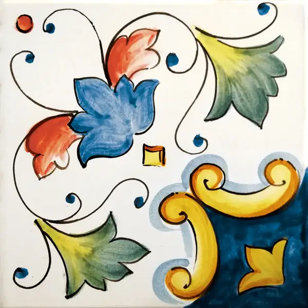 Mattonella decorata con un fiore blu con petali rossi, foglie verdi e volute gialle su fondo bianco con un angolo blu