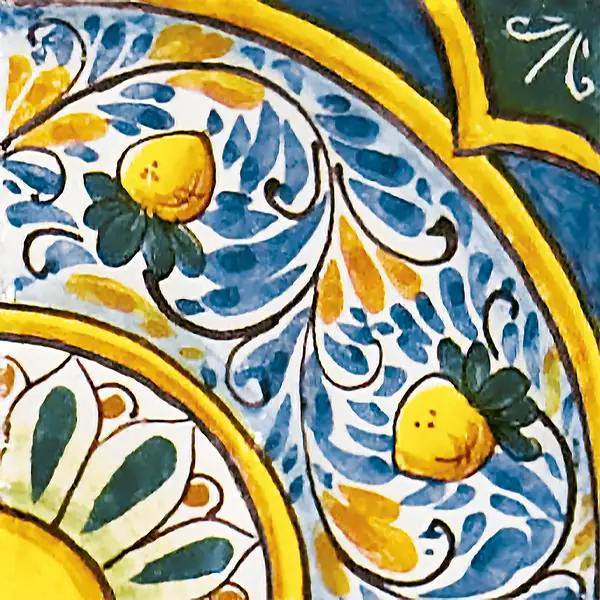 Mattonella decorata con limoni gialli, foglie e piccoli motivi blu lungo fasce curve, con contorni gialli e settori blu e verdi