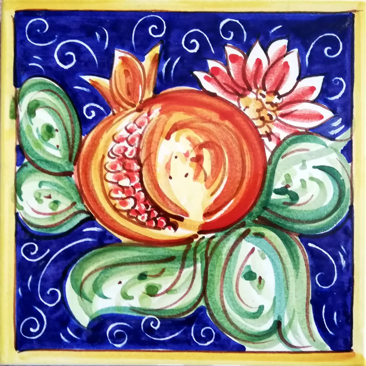 Mattonella decorata con melograno aperto, foglie verdi e fiore bianco e rosso su fondo blu