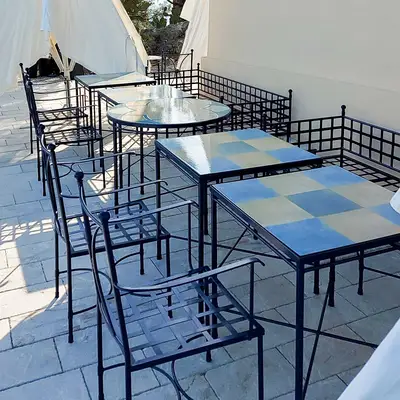 Tavoli quadrati in pietra lavica con decori geometrici blu e sedie in ferro su una terrazza
