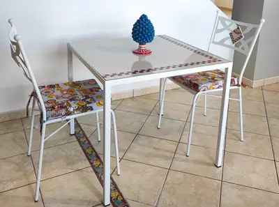 Tavolo quadrato con inserti in pietra lavica chiara e sedie bianche con sedute decorate