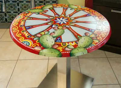Tavolo rotondo in pietra lavica Ruota Carretto Sicilia, con base in acciaio e ruota colorata al centro del piano.