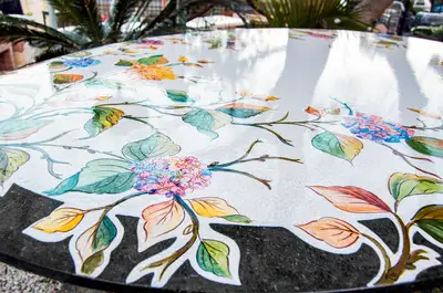 Dettaglio del piano ovale in pietra lavica a decoro floreale, vista ravvicinata dei fiori e della superficie lucida.